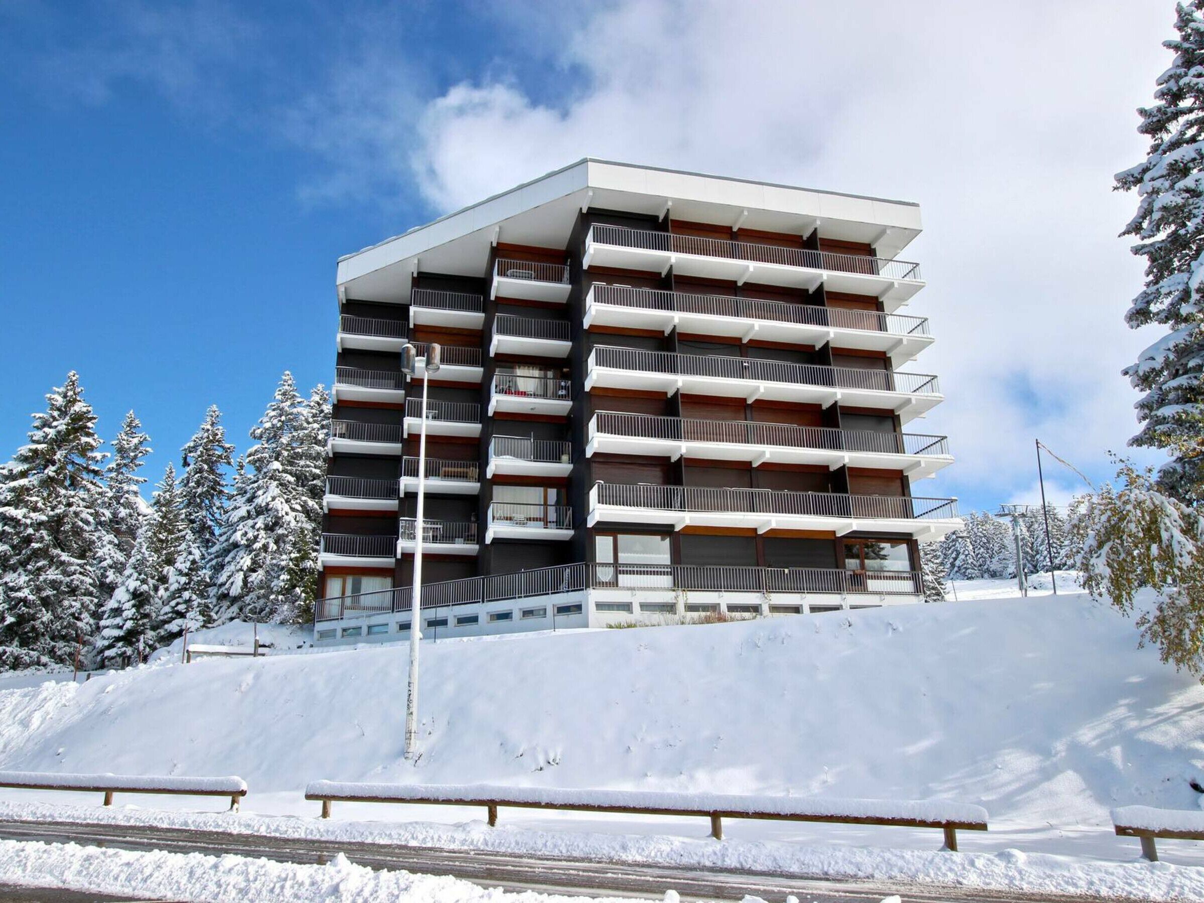 A multi-story building with balconies, surrounded by snow-covered trees and a clear sky.