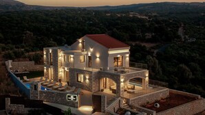 Eine moderne Villa mit Naturstein-Fassade, einem Pool und einem Balkon mit Blick auf eine hügelige Landschaft.