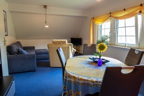 Un salon comprenant un canapé, une table à manger avec des chaises, un téléviseur et une fenêtre avec des rideaux.