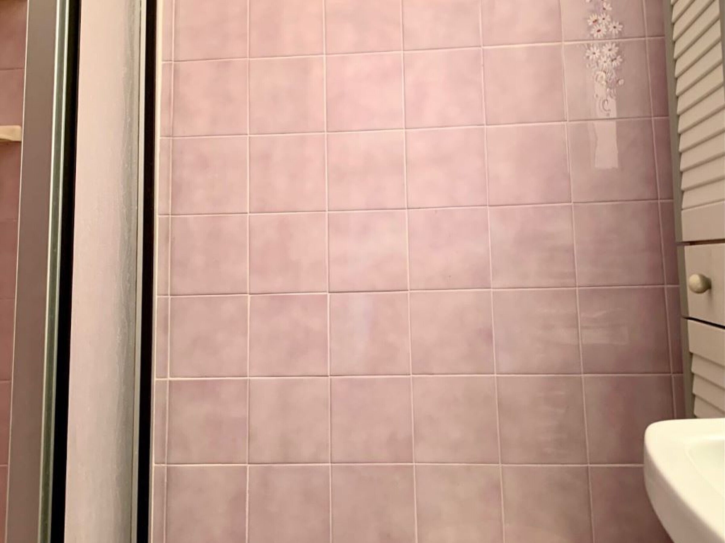 Un bagno con piastrelle rosa, un lavandino bianco e una porta con maniglia.