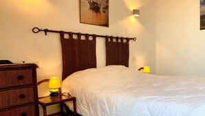 Ein ordentlich bezogenes Bett mit weißer Bettdecke, eine hölzerne Kommode mit Schubladen, ein kleiner Nachttisch mit Lampe und ein an der Wand befestigter Schlüssel.