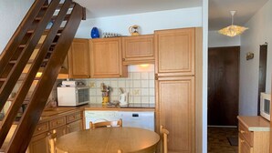Eine kleine Küche mit Holzschränken, einem Esstisch und einer Treppe.