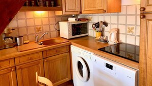 Eine kompakte Küche mit Holzausstattung, einer Mikrowelle, einer Waschmaschine und einem Spülbecken.