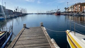 Eine hölzerne Mole, die in eine Marina führt, mit Booten und Gebäuden im Hintergrund.