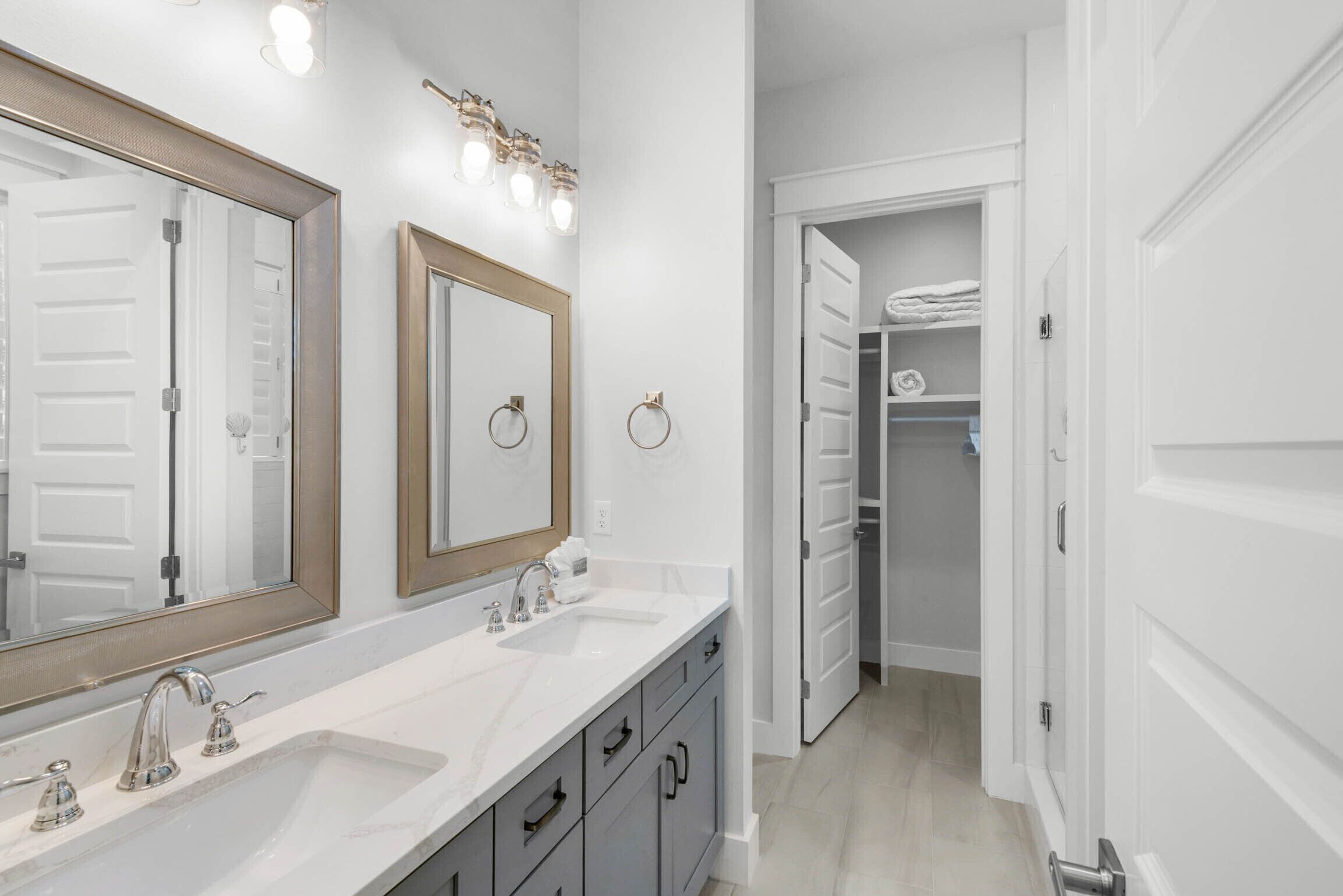 A modern bathroom with a double sink, large mirrors, and a walk-in closet.