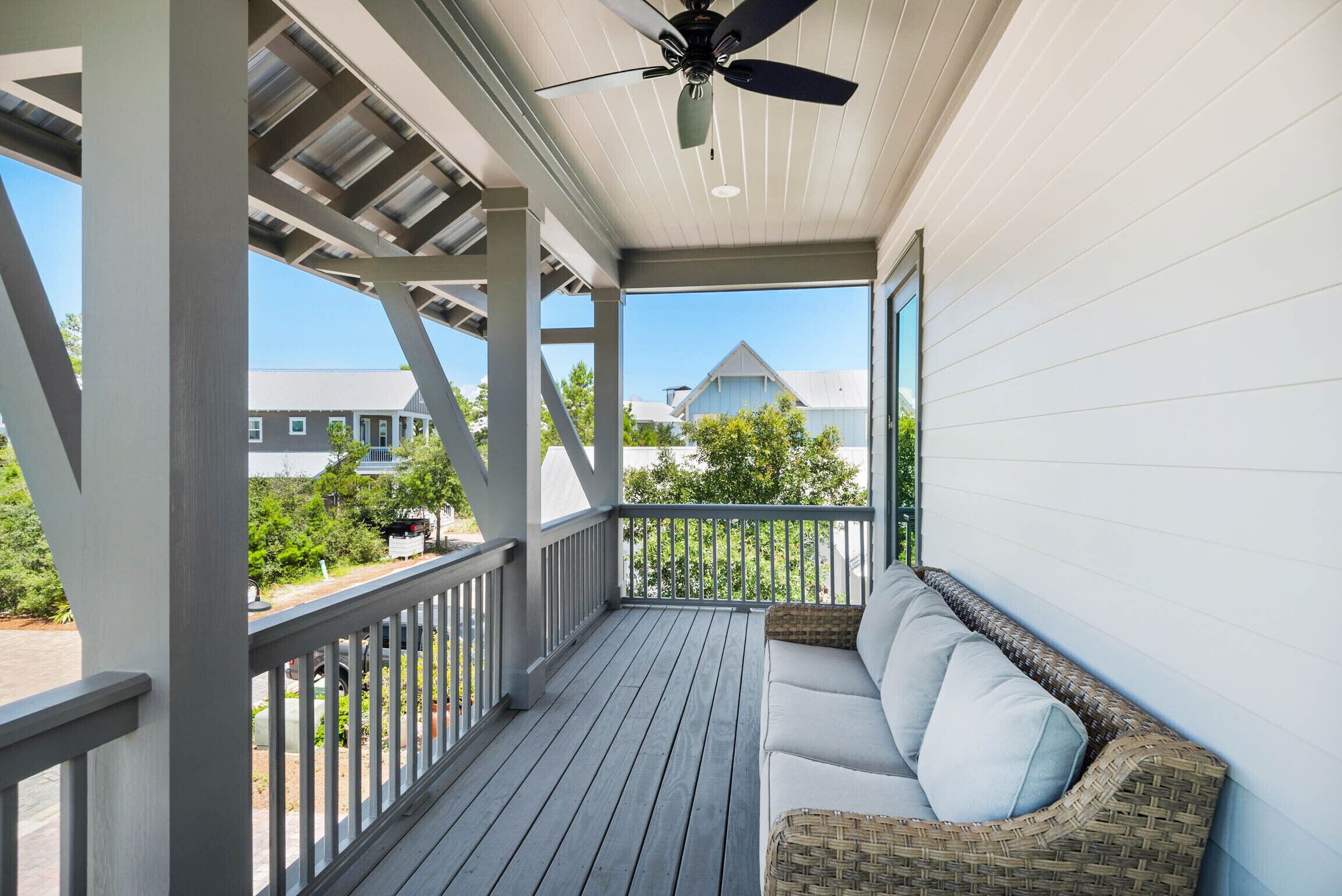 Eine überdachte Veranda mit weißer Reling, einem Deckenventilator und einem Korbsessel mit Kissen.