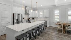 A modern kitchen with white cabinetry, a stainless steel refrigerator, a large island with bar stools, and pendant lighting. - ☀️Spacious Balcony-30A-2 Masters-Bikes-Blue Heron Hideaway (Santa Rosa Beach)