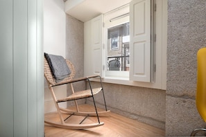 Een hoekkamer met een schommelstoel, een raam met geopende luiken en uitzicht op het balkon.