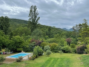 Una piscina rodeada de abundante vegetación y árboles, con un paisaje montañoso al fondo.