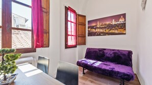 A room with a dining table, a purple sofa, a potted plant, and a cityscape painting on the wall.
