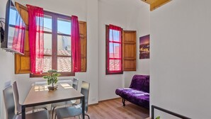 A room with a dining table, chairs, a purple sofa, and a window with red curtains.