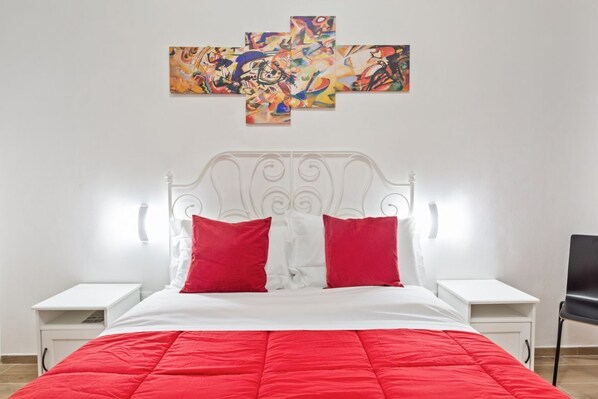 A bed with a white headboard and red bedding, two bedside tables, and a wall with abstract art.