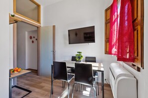 A compact living space with a dining area, a flat-screen TV mounted on the wall, and a window with a red curtain. - GuestHost - Comfortable 35sqm apartment that can accommodate up to 4 people. Located on the second floor, without a lift, of a building 3 minutes walk away from Uffizi Gallery and Piazza della Signoria, the accommodation is the best solution to visit the (Firenze)