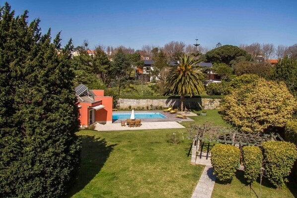 A residential property with a swimming pool, a patio with seating, and a well-maintained lawn.