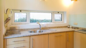 A kitchen with a granite countertop, stainless steel sink, wooden cabinets, and a window above the sink. - Garden Pool House by Liiiving (Porto)