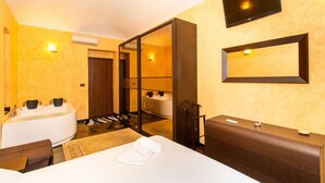Una camera d'albergo con un letto, una scrivania, uno specchio, una TV, una vasca e una doccia.