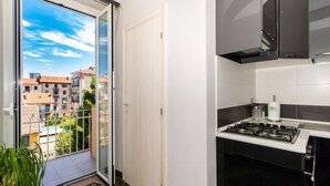 Cucina con piano cottura a gas, un piccolo bancone e vista sugli edifici attraverso una porta vetrata.