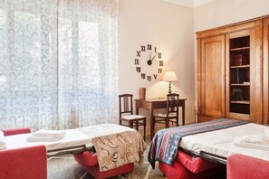 Une chambre avec deux lits, un bureau, une chaise, une lampe et une grande armoire en bois.
