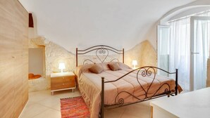 A bedroom with a bed, bedside tables, a nightstand, a rug, and a window with curtains. - GuestHost - Lovely apartment located in the heart of Monopoli, in the historic center, in a stone building of which it retains suggestive evidences in the internal architecture. The flat can comfortably accommodate two people and is located in an enviabl (Monopoli)