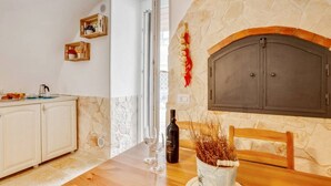 A kitchen with a stone fireplace, wooden cabinets, a dining table with wine glasses, and a clock on the wall. - GuestHost - Lovely apartment located in the heart of Monopoli, in the historic center, in a stone building of which it retains suggestive evidences in the internal architecture. The flat can comfortably accommodate two people and is located in an enviabl (Monopoli)