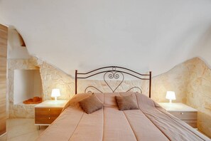 Een slaapkamer met een stenen muur, een bed met hoofdeinde, twee nachtkastjes met lampen en een houten nachtkastje.