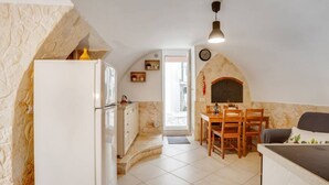 A compact kitchen with a stone wall, a white refrigerator, a dining table with chairs, and a built-in oven. - GuestHost - Lovely apartment located in the heart of Monopoli, in the historic center, in a stone building of which it retains suggestive evidences in the internal architecture. The flat can comfortably accommodate two people and is located in an enviabl (Monopoli)