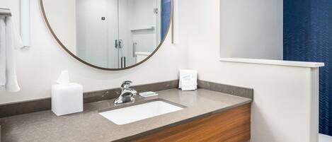 A bathroom with a round mirror, a sink, and a towel dispenser.