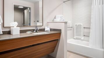A modern bathroom with a wooden vanity, a large mirror, a white sink, and a separate shower area.