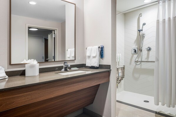 Un baño moderno con tocador de madera, un espejo grande, ducha con puerta de vidrio y un perchero para toallas.