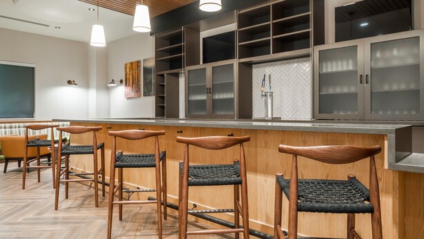 A modern bar area with wooden stools and a counter, featuring built-in shelves and a large mirror.