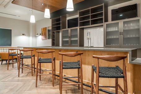 A modern bar area with wooden stools and a counter, featuring built-in shelves and a large mirror.