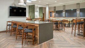 A modern restaurant with a central bar area, multiple seating options, and a large flat-screen TV mounted on the wall.