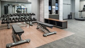 A gym with weightlifting equipment, benches, and a mirrored wall.