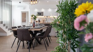 A modern dining area with a wooden table and chairs, a kitchen in the background, and a vertical garden with flowers. - New Luxury Modern Four-bedroom Villa With Pool (Kastela)