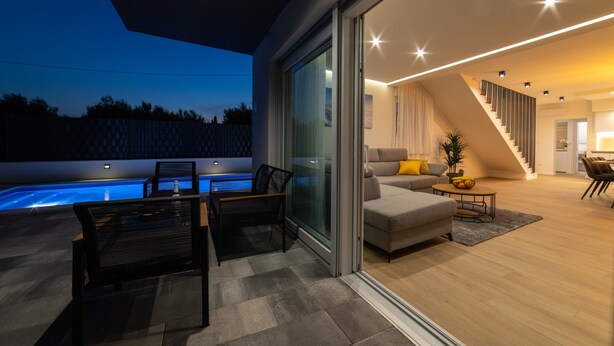 A modern living room with a sofa, coffee table, and a pool area visible through glass doors. - New Luxury Modern Four-bedroom Villa With Pool (Kastela)