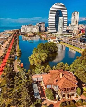 A modern cityscape with a distinctive curved building, a waterfront promenade, and a traditional building with a tiled roof.