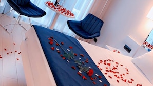 A hotel room with a bed, two chairs, a table with a bottle, and rose petals scattered on the floor. - Orbi City Batumi Apartment With sea Views (Batumi)