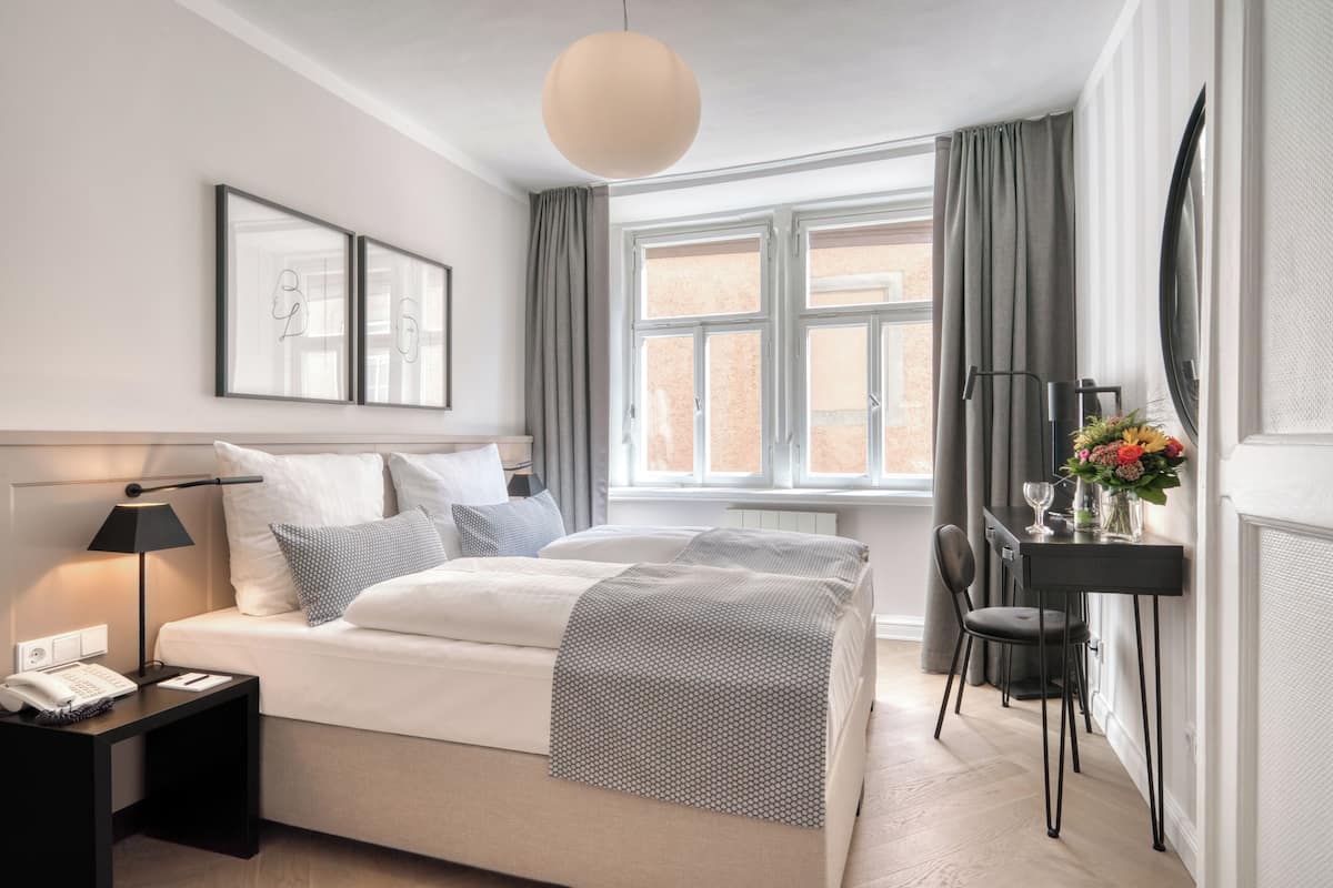 A modern bedroom with a bed, bedside table, lamp, and a window with curtains.