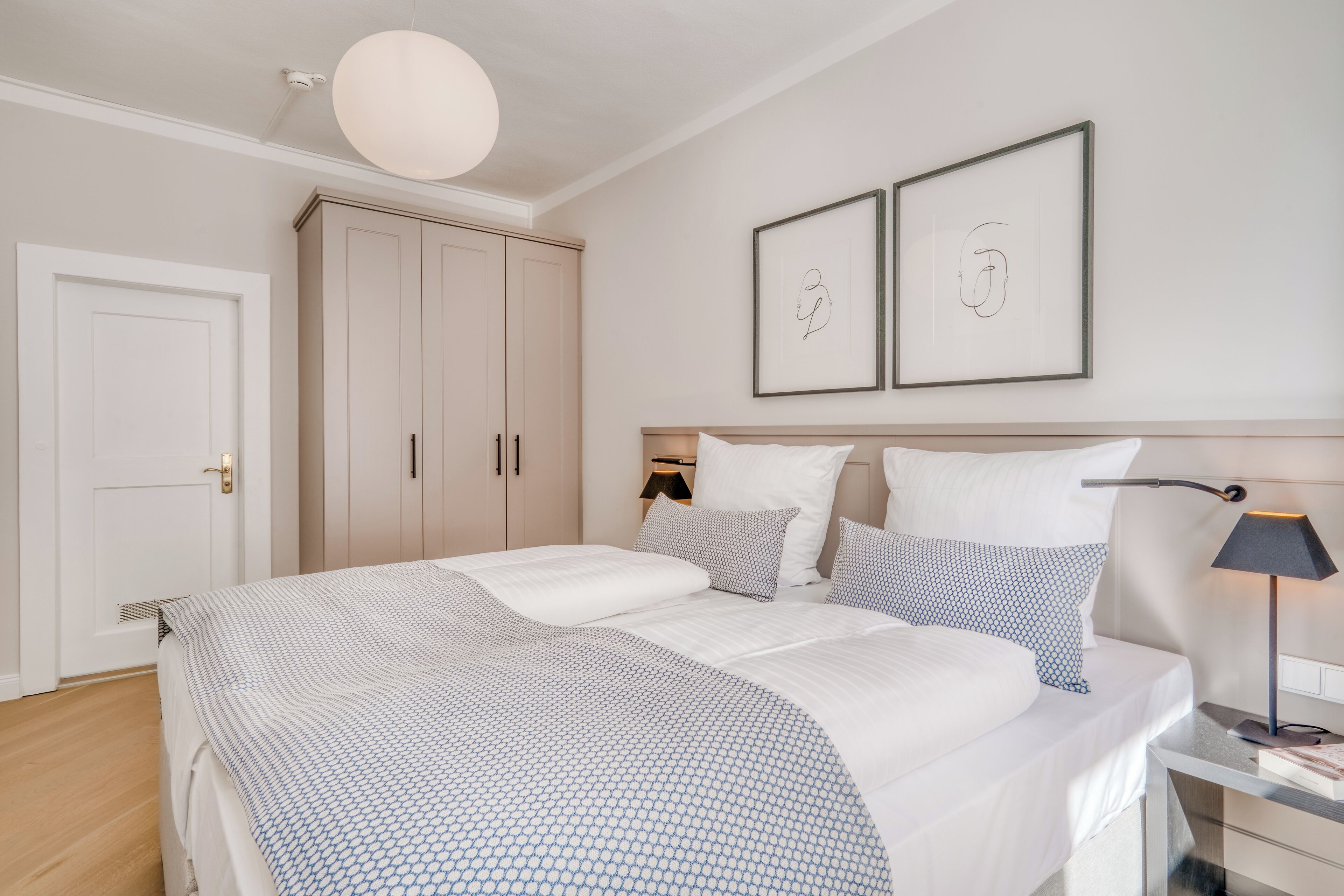 A bedroom with a bed, bedside tables, a lamp, a wardrobe, and two framed pictures on the wall.