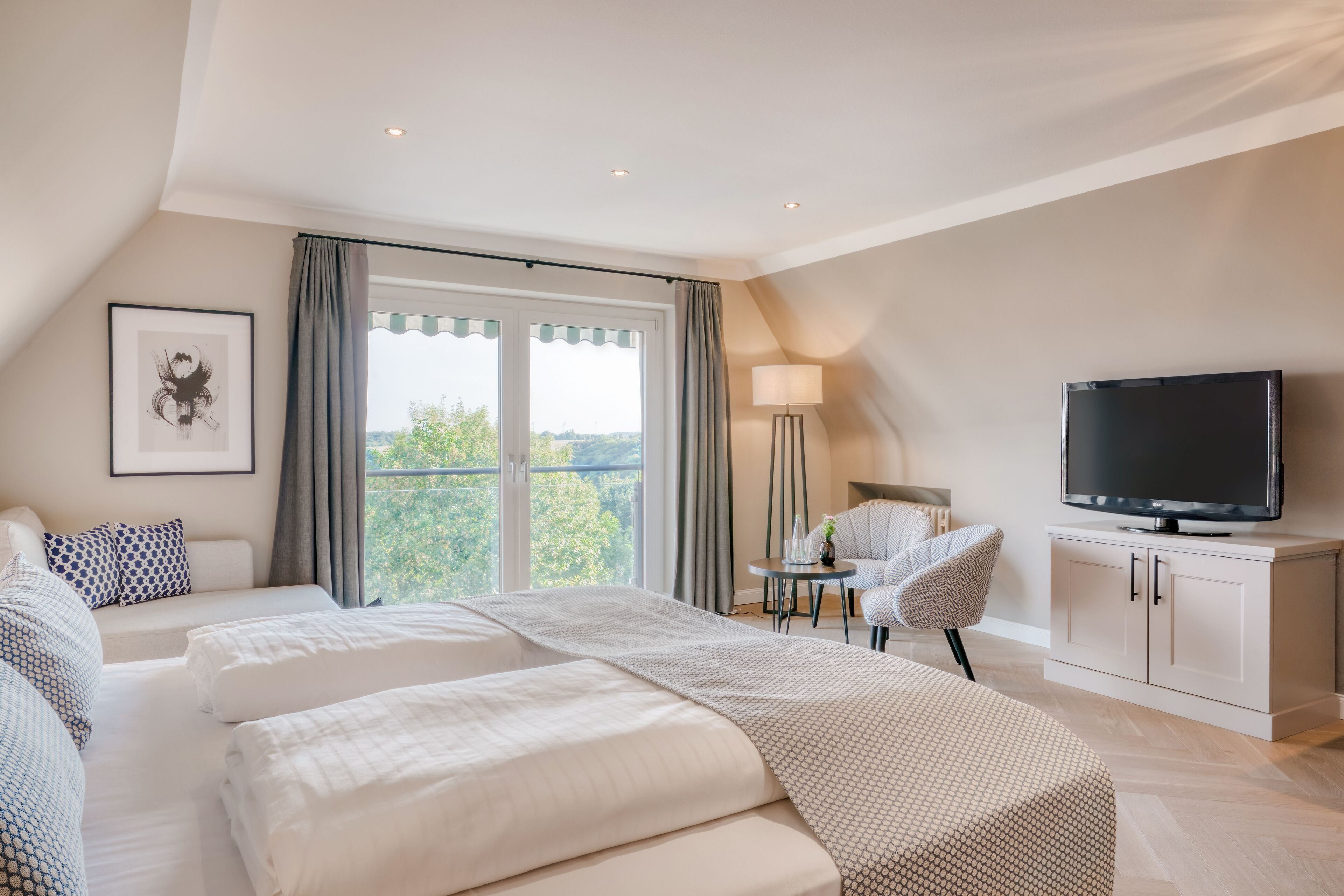 Ein modernes Hotelzimmer mit zwei Betten, einem Fernseher, einem Schreibtisch und Blick ins Freie.