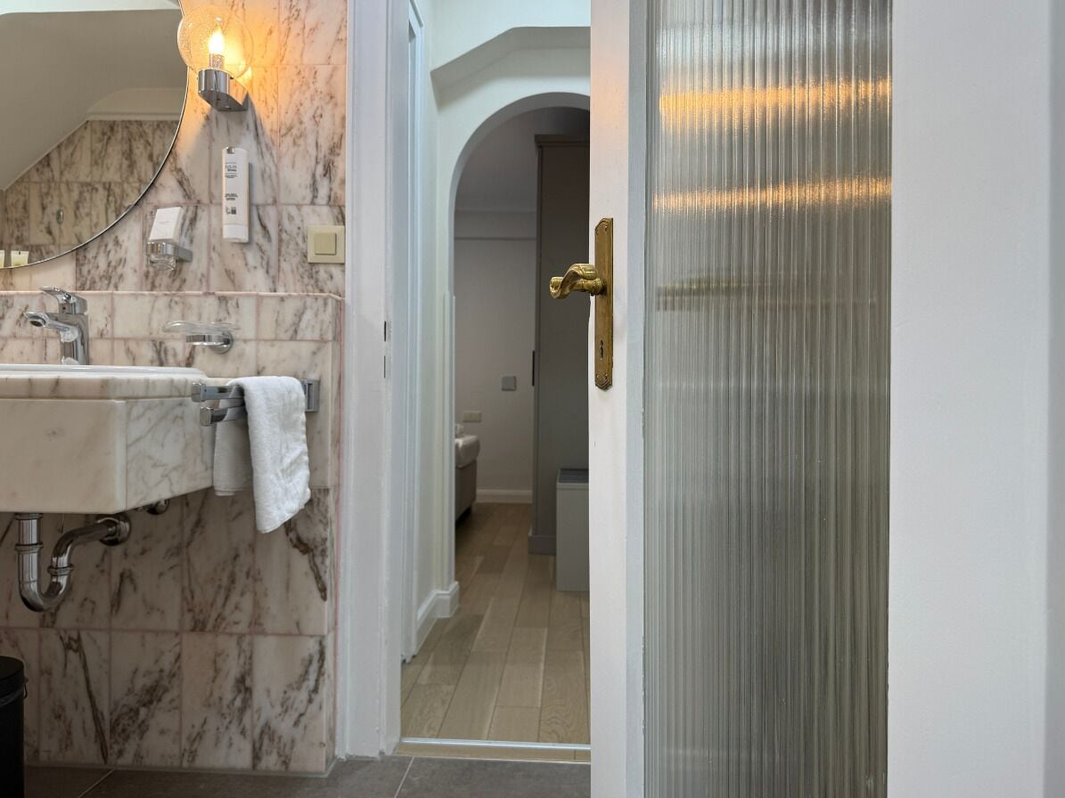 Un baño con lavamanos de mármol, una toalla, una lámpara y una puerta que da a otra habitación.