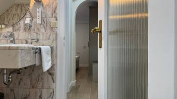 A bathroom with a marble sink, a towel, a light fixture, and a door leading to another room.