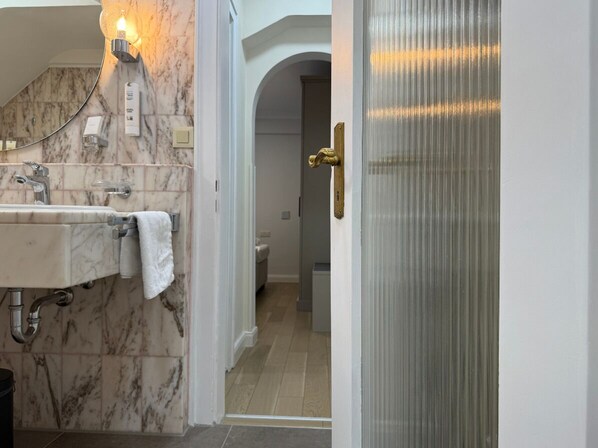 A bathroom with a marble sink, a towel, a light fixture, and a door leading to another room. - Hotel Eisenhut (Rothenburg ob der Tauber)