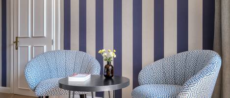 Una habitación con dos sillones estampados, una mesita redonda con un florero y una puerta con rayas verticales.