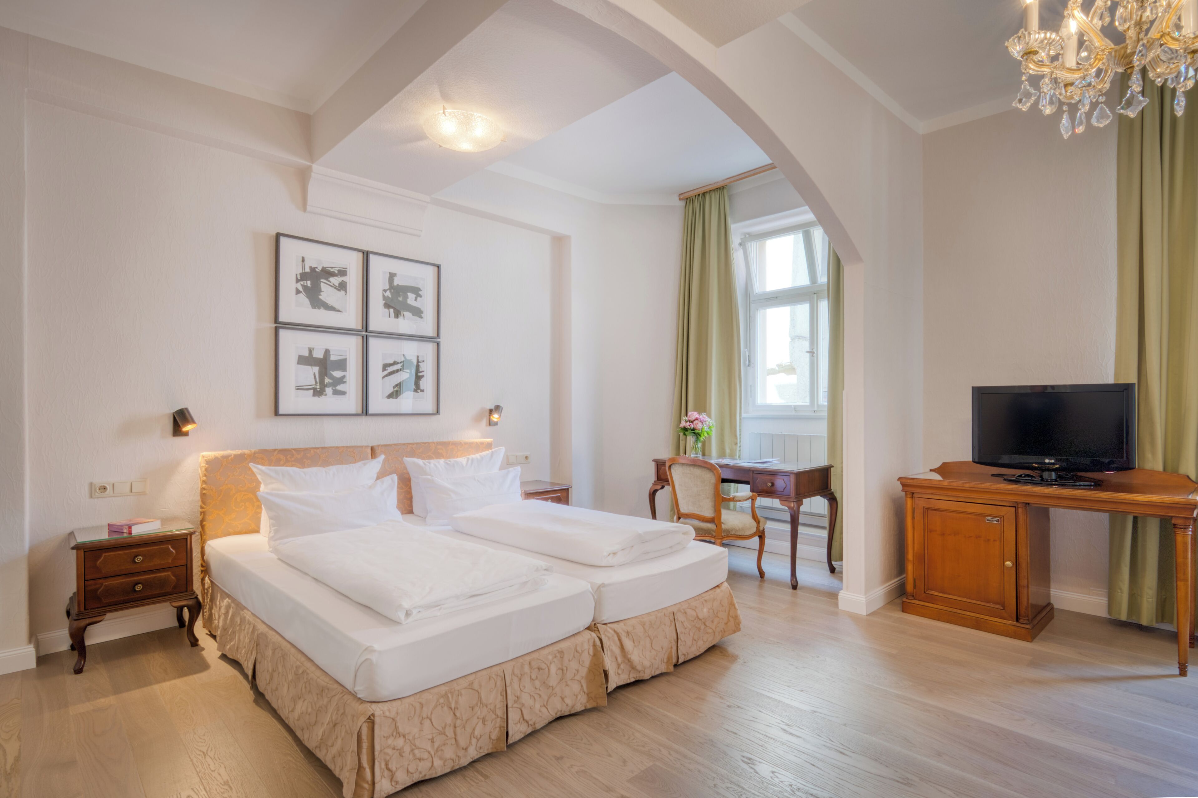 A hotel room with a large bed, a desk, a television, and artwork on the wall.
