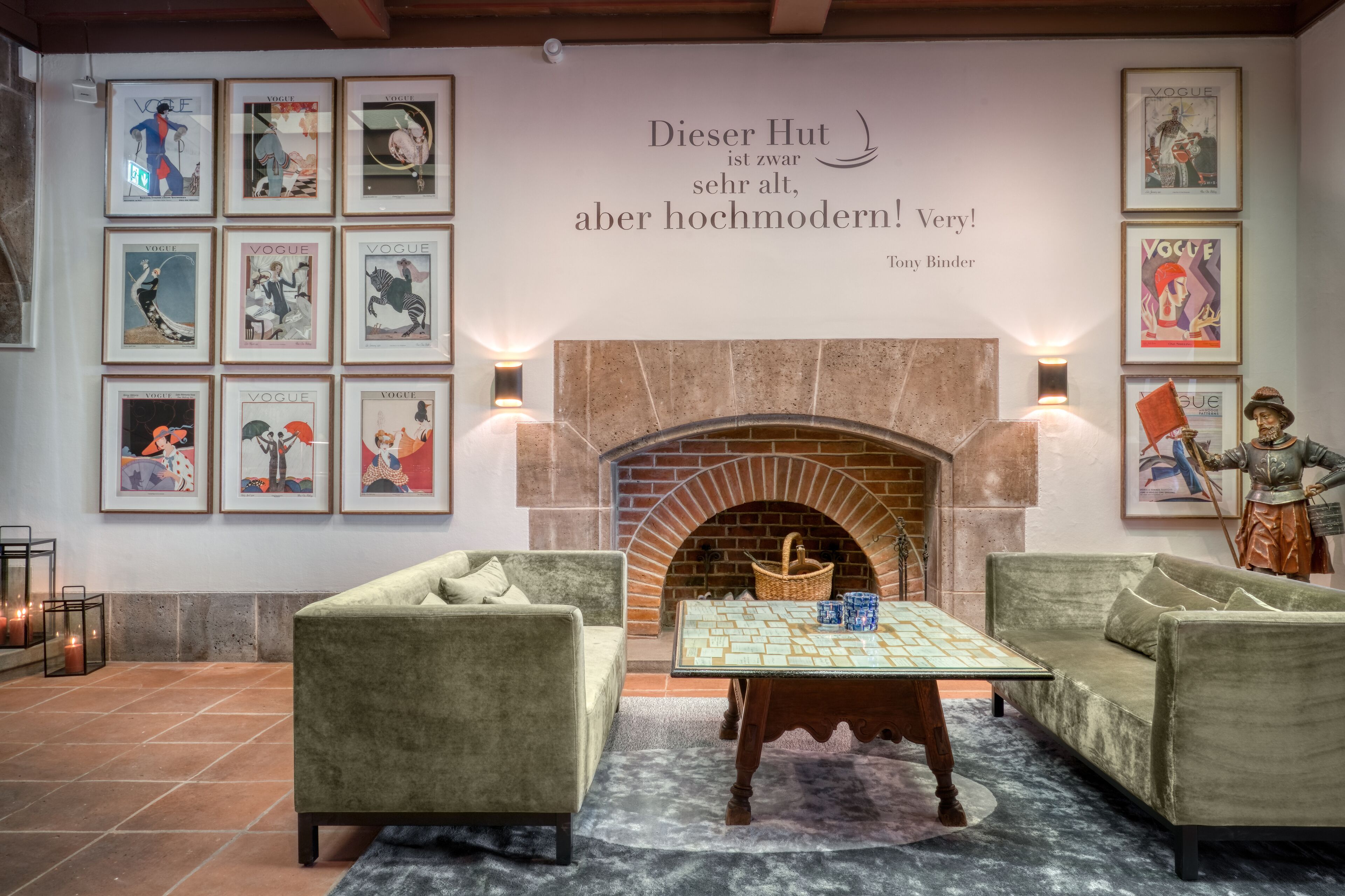 A cozy lounge area with a fireplace, framed magazine covers on the wall, and a vintage statue.