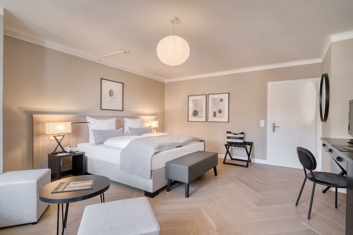 A modern hotel room with a large bed, bedside tables, a desk, and a chair.