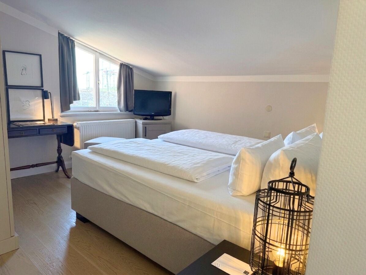 A bedroom with a bed, a desk with a computer, a television, and a window with curtains.