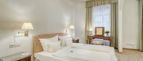 Une chambre d’hôtel avec un grand lit, deux tables de chevet, une commode, un miroir et une fenêtre avec des rideaux.