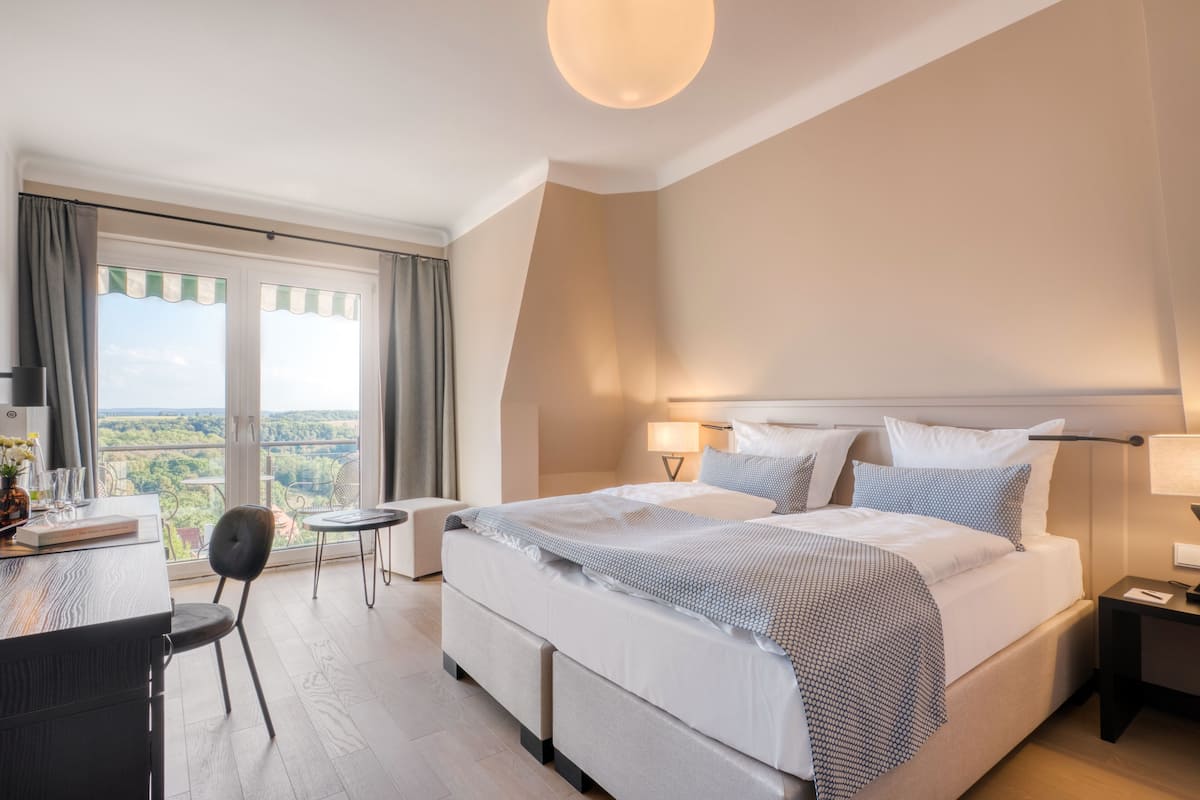 A modern hotel room with a large bed, bedside tables, a desk, and a view of the outdoors.